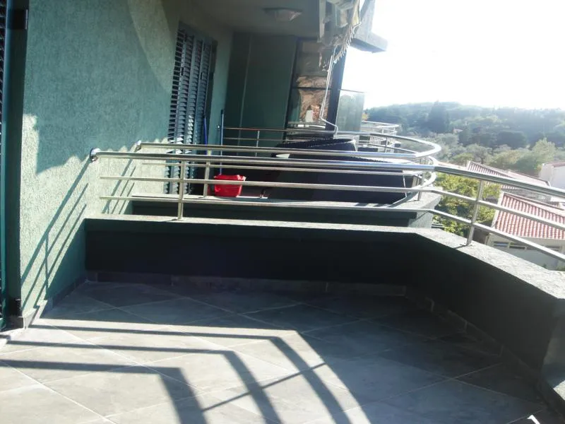 Przestronny balkon z płytkami i metalową balustradą w mieszkaniu, Miločer, Czarnogóra, widok na zielone wzgórza.
