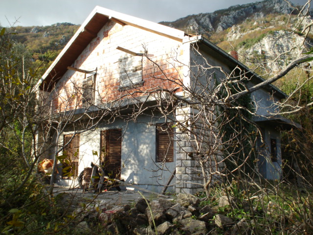 Dwupiętrowy dom do rekonstrukcji na działce w Herceg Novi, Czarnogóra, na tle górskiego krajobrazu.
