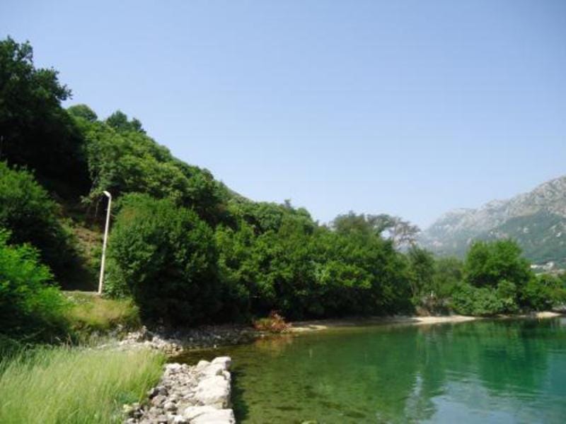 Građevinsko zemljište uz more u Kostanjici, Crna Gora: pogled na obalu, zelene brežuljke i planine u Bokokotorskom zalivu.