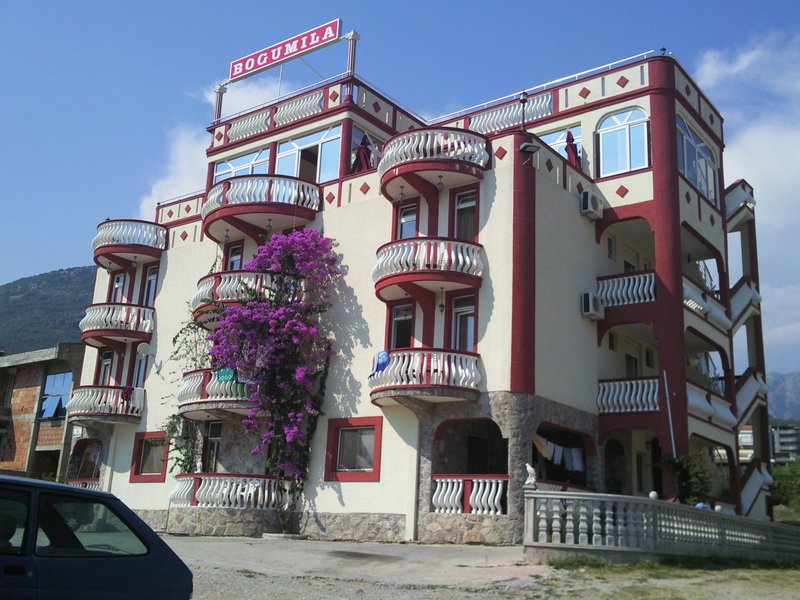 Fasada hotelu Bogumila w mieście Bar, Czarnogóra: czteropiętrowy budynek z półokrągłymi balkonami i kwitnącą bugenwillą.