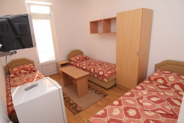 Pokój trzyosobowy w hotelu w mieście Bar, Czarnogóra: trzy łóżka, szafa, lodówka, telewizor i wyjście na balkon.