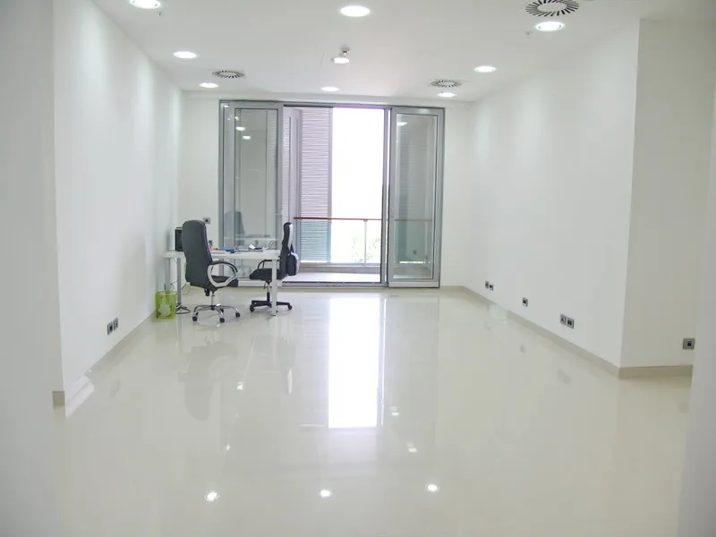 Spacious white office room with a desk, two chairs, and a balcony door.