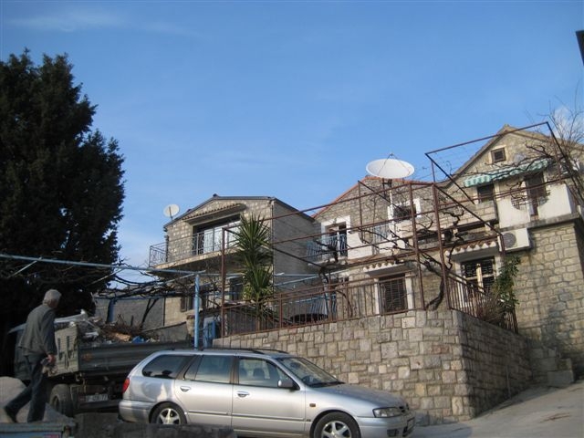 Karadağ, Rafailovići’de teraslı, üzüm asmalı ve park edilmiş araçlı iki katlı taş ev.