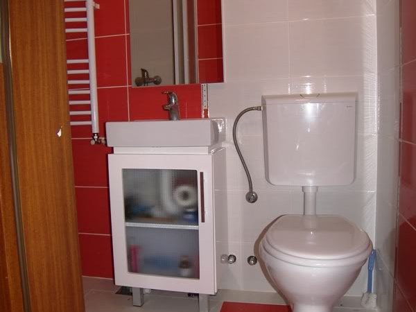 Karadağ, Budva’daki evde banyo: beyaz sıhhi tesisat, lavabolu dolap ve kırmızı fayans duvar kaplaması.
