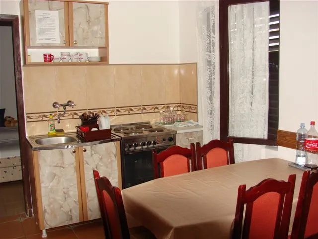 Küche mit Essbereich in einem Haus in Budva, Montenegro: Herd, Spüle, Holztisch und Stühle mit roter Polsterung.