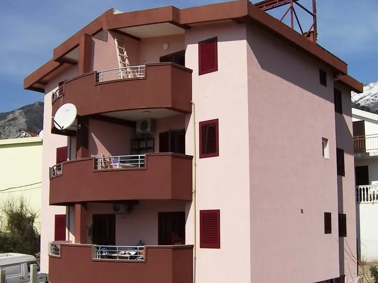 Dreistöckiges Wohnhaus mit Balkonen in Budva, Montenegro: Fassade in rosa-braunen Tönen mit Blick auf die Berge.