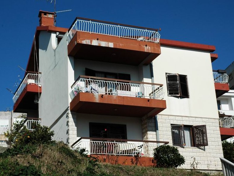 Dreistöckiges Haus in Herceg Novi, Montenegro: Fassade mit Terrassen, weißer Verkleidung und Steinsockel vor dem Himmel.