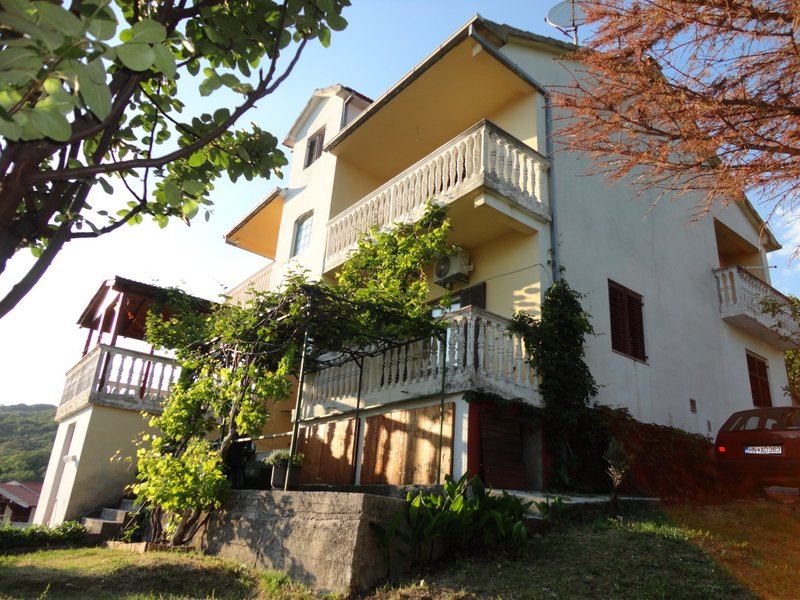 Dreistöckiges Haus in Herceg Novi, Montenegro, mit Terrassen, Balustraden, Weinreben und einem Garten vor der Fassade.