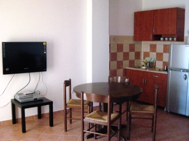 Karadağ, Budva’daki villa dairesinde mutfak-yemek odası: yemek alanı, ahşap mutfak takımı ve TV alanı.