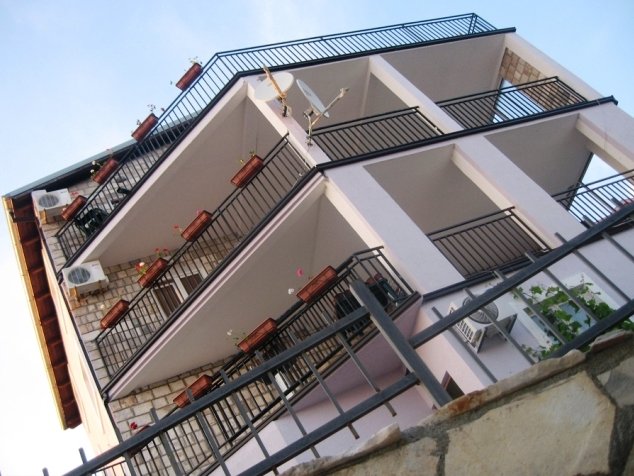 Karadağ, Budva’da üç katlı villa: taş kaplamalı ve korkuluklu açık balkonlara sahip binanın alttan görünümü.