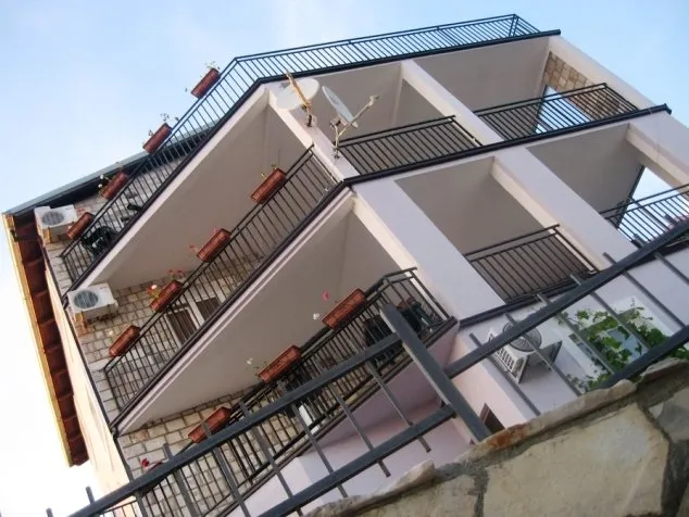 Dreistöckige Villa in Budva, Montenegro: Blick von unten auf das Gebäude mit Steinverkleidung und offenen Balkonen mit Geländern.