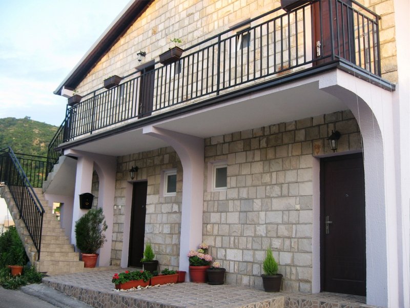 Karadağ, Budva’daki iki katlı villanın cephesi: taş kaplama, açık teras, balkon ve dış merdiven.