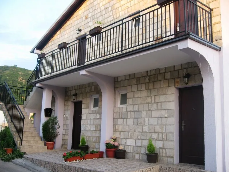 Fassade einer zweistöckigen Villa in Budva, Montenegro: Steinverkleidung, offene Terrasse, Balkon und Außentreppe.