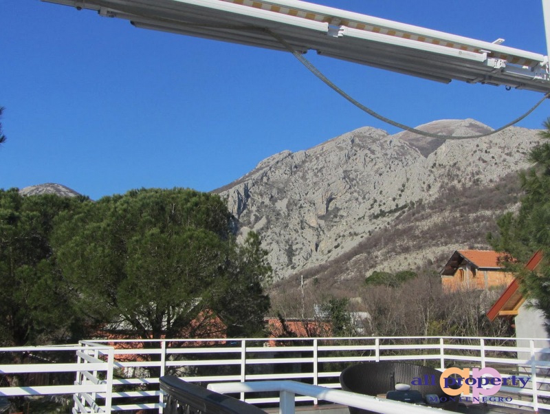 View from the balcony of a house in Bar, Montenegro: a panorama of mountains, coniferous trees, and a white terrace railing.