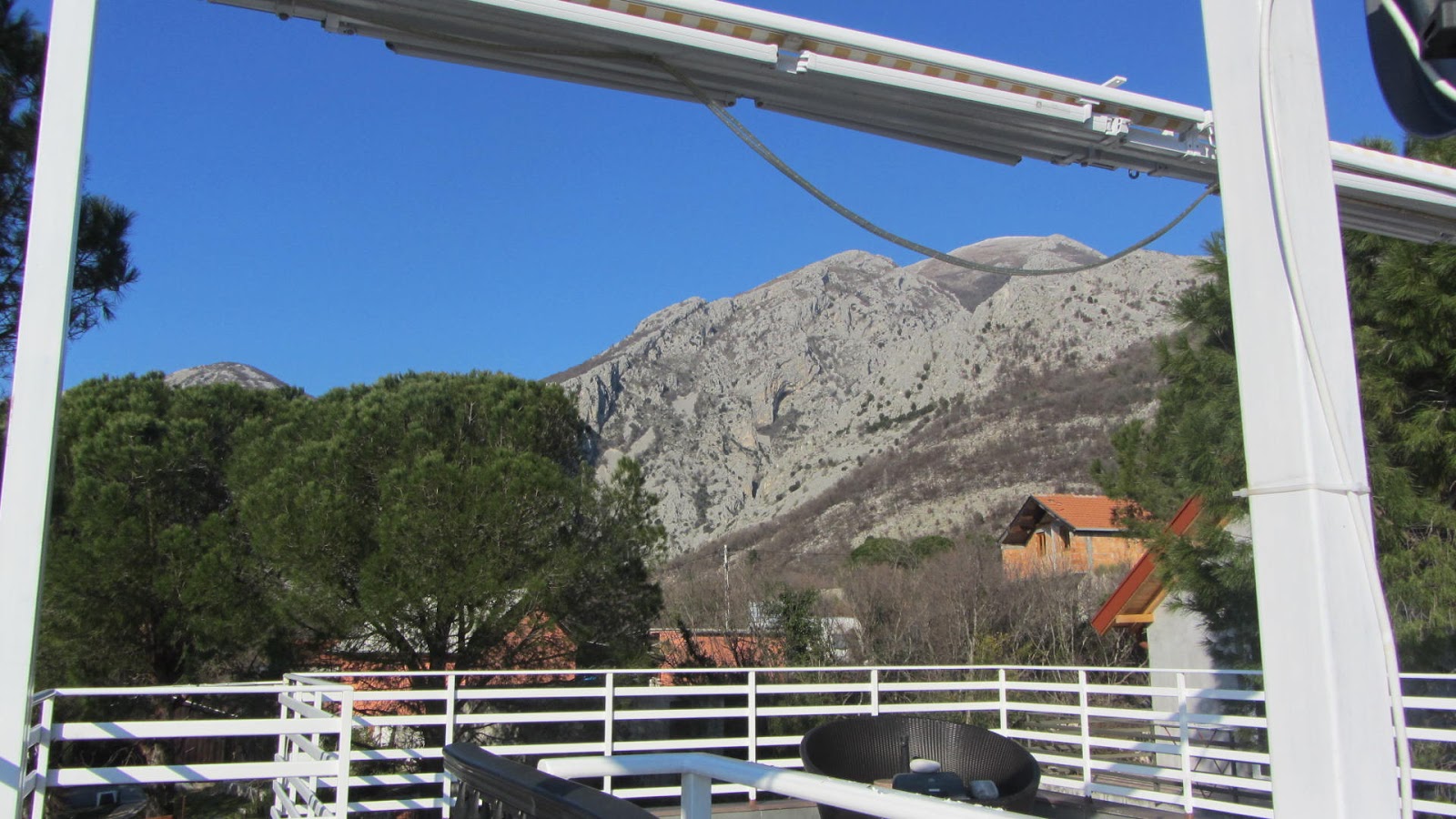 View from the balcony of a house in Bar, Montenegro: a panorama of mountains, pine trees, and a white terrace railing with garden furniture.