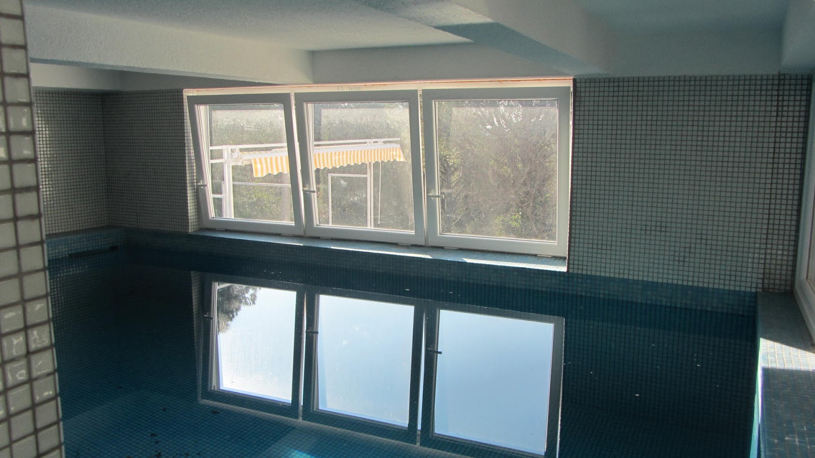 Indoor pool finished with blue mosaic in a house in Bar, Montenegro, with a panoramic window and garden view.