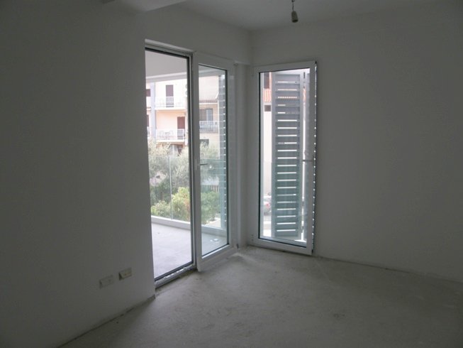 Salon lumineux dans une résidence neuve à Pržno, Monténégro : murs blancs, baies vitrées panoramiques avec stores et accès à la terrasse.