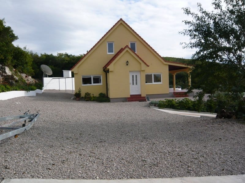 Zweistöckiges gelbes Einfamilienhaus mit Terrasse und Kieshof in Nikšić, Montenegro.