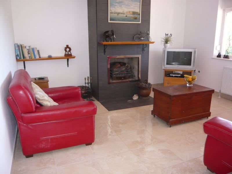 Wohnzimmer in einem Haus in Nikšić, Montenegro: rote Ledersessel, Kamin mit dunkler Verkleidung und heller Fliesenboden.