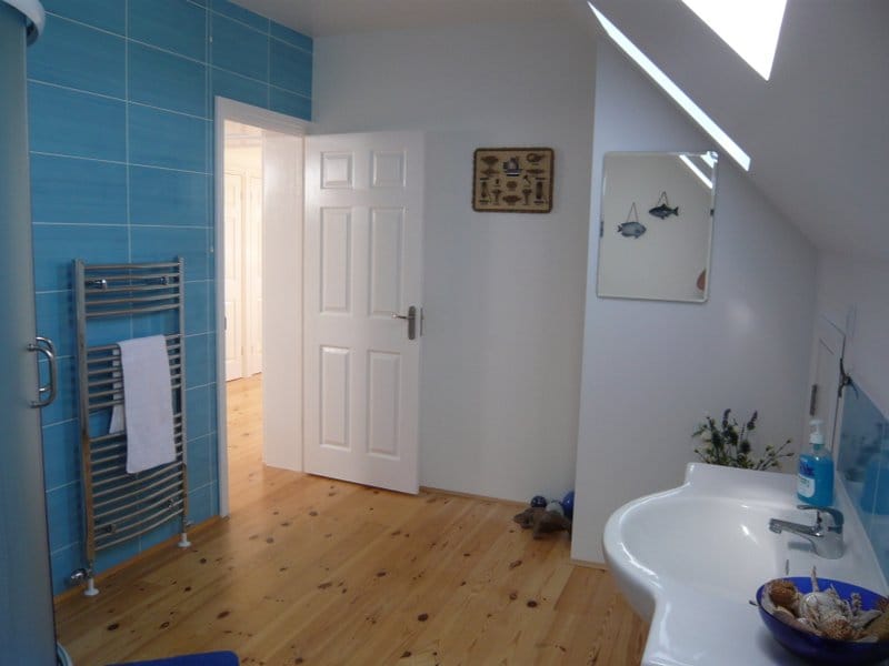 Helles Badezimmer in einem Haus in Nikšić, Montenegro: Holzboden, blaue Fliesen, Waschbecken und Dachfenster.