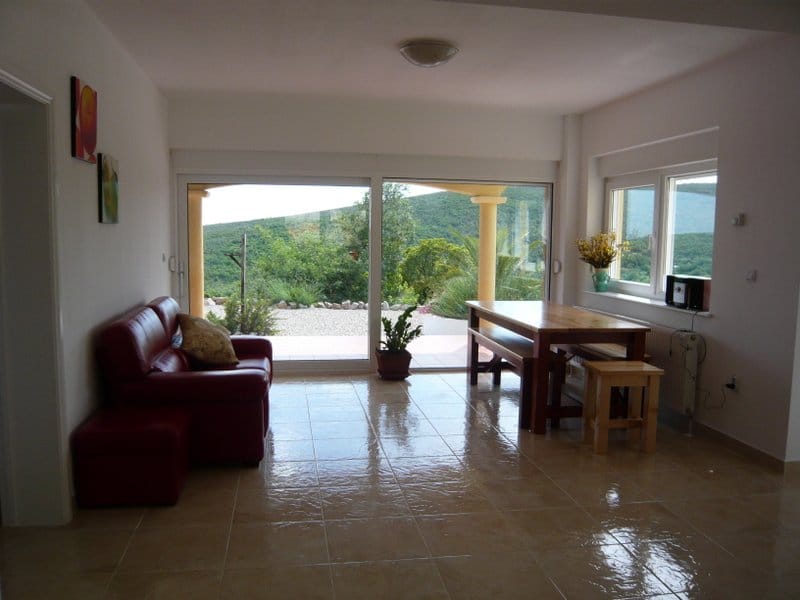 Wohnzimmer in einem Haus in Nikšić, Montenegro: rotes Sofa, Holztisch, Panoramafenster mit Blick auf die Berge und die Terrasse.