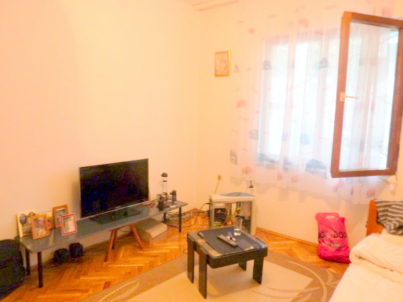 Wohnzimmer in einem Haus in Sutomore, Montenegro: heller Raum mit Parkettboden, TV-Bereich und einem Fenster mit leichten Vorhängen.
