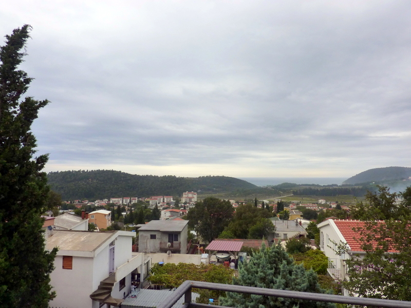 Panoramablick vom Balkon eines Hauses in Sutomore, Montenegro: grüne Hügel, niedriggeschossige Bebauung und der Meereshorizont.