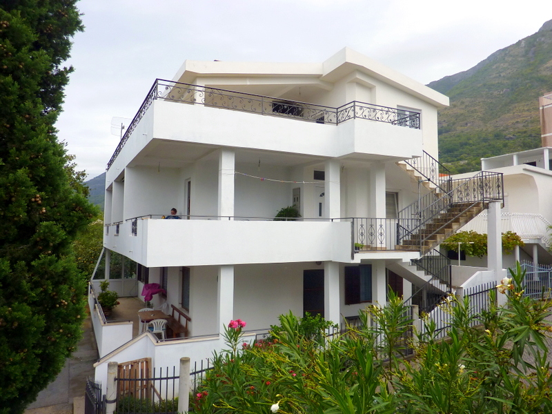 Dreistöckiges weißes Haus mit Terrassen und Außentreppe in Sutomore, Montenegro, umgeben von viel Grün und Bergen.