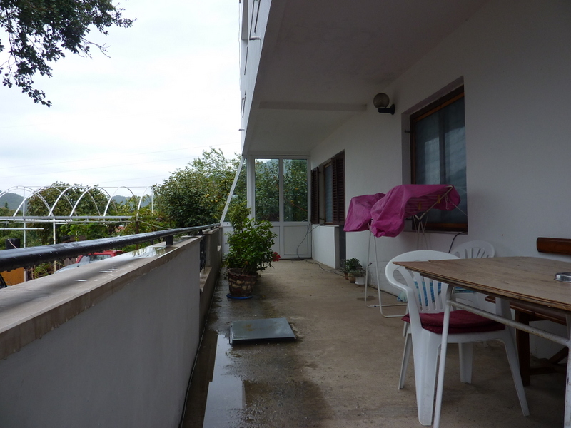 Geräumiger Balkon eines Hauses in Sutomore, Montenegro: Holztisch, Kunststoffstühle und Blick auf einen grünen Garten.