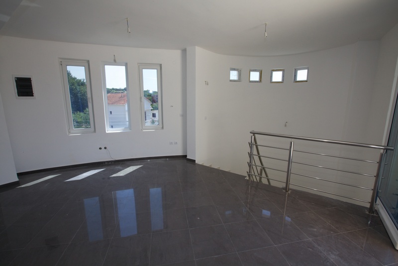 Helles Wohnzimmer in einem Haus in Utjeha, Montenegro: grauer Fliesenboden, weiße Wände, Panoramafenster und eine Treppe mit Geländer.