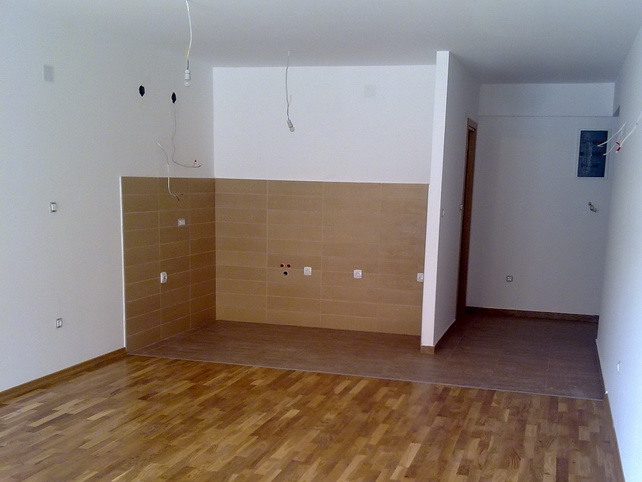 Küche in einer neuen Wohnung in Budva, Montenegro: helle Ausstattung, Fliesenspiegel und verlegter Parkettboden.