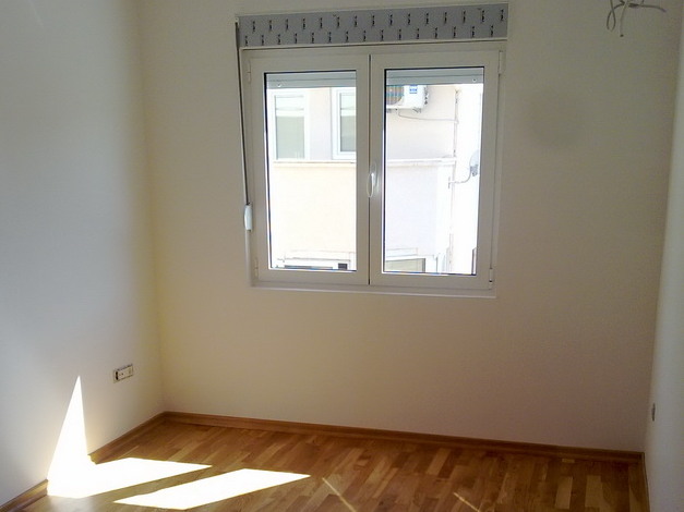Helles Schlafzimmer mit Parkettboden und Kunststofffenster in einer zum Verkauf stehenden Wohnung in Budva, Montenegro.