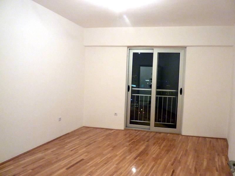 Helles Wohnzimmer mit Parkettboden und Zugang zum Balkon in einer Wohnung in Bečići, Montenegro. Leerer Raum zur Renovierung.