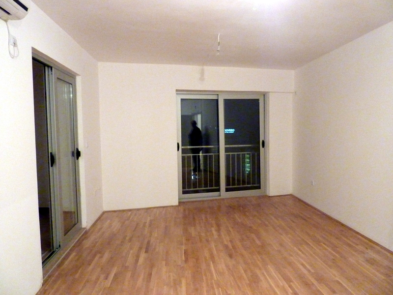 Helles Wohnzimmer mit Laminat und Panoramafenstern in einer Wohnung in Bečići, Montenegro. Blick auf den Balkon und die nächtliche Stadt.