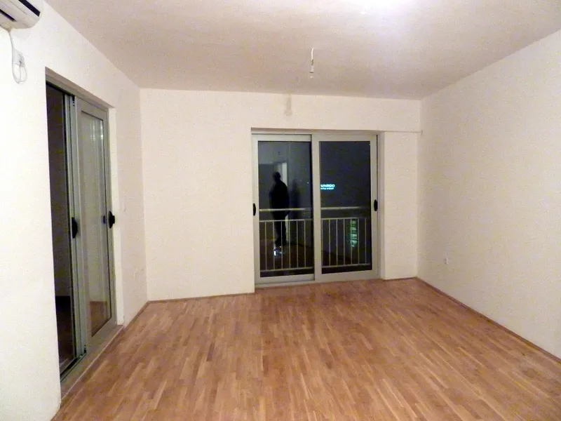 Helles Wohnzimmer mit Laminat und Panoramafenstern in einer Wohnung in Bečići, Montenegro. Blick auf den Balkon und die nächtliche Stadt.