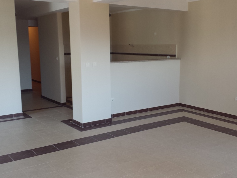 Geräumiges Wohnzimmer mit Fliesenverkleidung in einer zum Verkauf stehenden Wohnung in Pržno, Montenegro: Blick auf den Küchenbereich und den Flur.