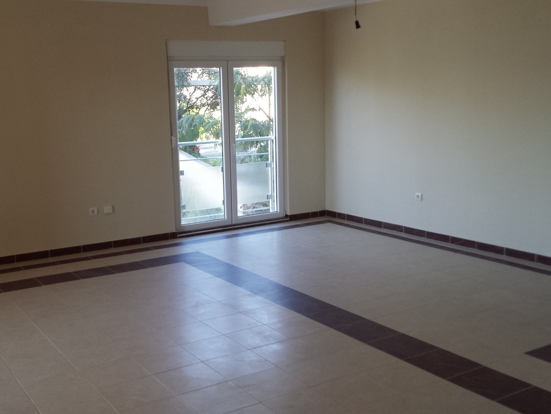 Helles Wohnzimmer in einer Wohnung in Pržno, Montenegro: Fliesenboden, weiße Wände und Zugang zum Balkon mit Blick ins Grüne.