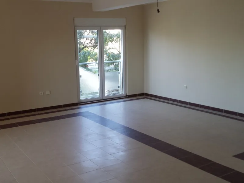 Helles Wohnzimmer in einer Wohnung in Pržno, Montenegro: Fliesenboden, weiße Wände und Zugang zum Balkon mit Blick ins Grüne.