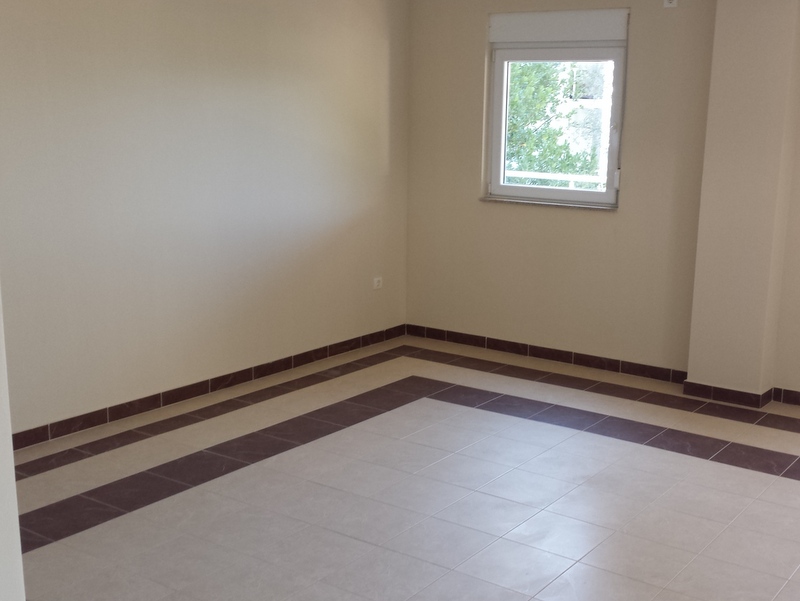 Helles Wohnzimmer in einer Wohnung in Pržno, Montenegro: Fliesenboden, beige Wände und ein Fenster mit Blick ins Grüne.