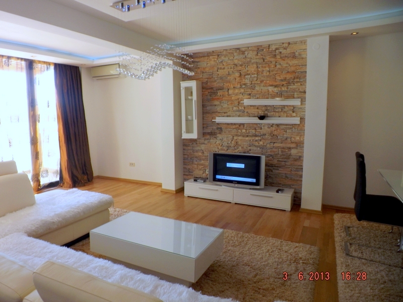 Wohnzimmer in einer Wohnung in Pržno, Montenegro: helle Möbel, Wandverkleidung mit dekorativem Stein und Panoramafenster.