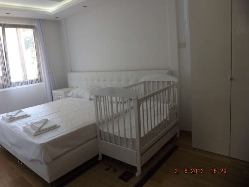 Helles Schlafzimmer mit Doppelbett und Babywiege in einer Wohnung in Pržno, Montenegro, mit modernem Interieur.