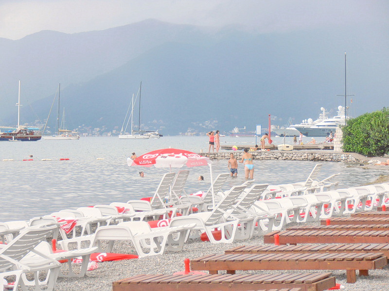 Plaža hotela u Tivtu, Crna Gora: beli ležaljke uz more, pogled na jahte, zaliv i planine u turističkoj zoni.