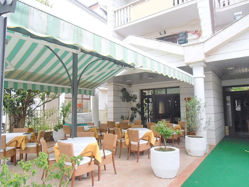 Außenterrasse eines Restaurants mit Tischen, Stühlen und Markisen.