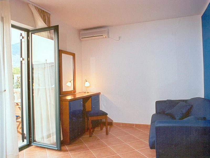 Enterijer dnevne sobe u hotelu u Tivtu, Crna Gora: plava sofa, toaletni stočić sa ogledalom i izlaz na balkon.