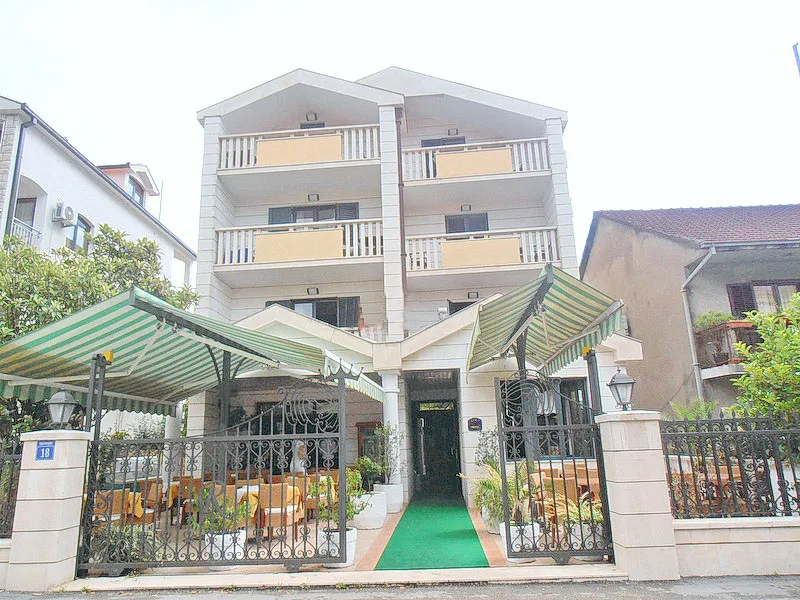 Fassade eines mehrstöckigen Hotels oder Wohngebäudes mit Balkonen und einer Restaurantterrasse im Erdgeschoss.