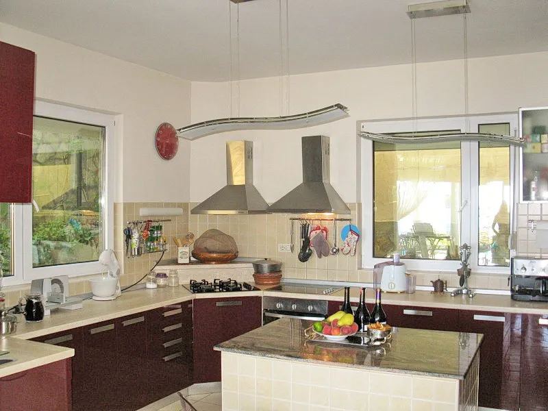 Modern kitchen with an island and appliances in a villa in Dobra Voda, Montenegro: burgundy fronts and a stone countertop.