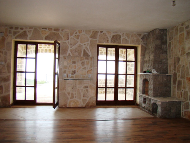 Petrovac, Karadağ’daki evde taş kaplamalı duvarlar ve şömineli oturma odası, panoramik kapılardan terasa çıkışlı