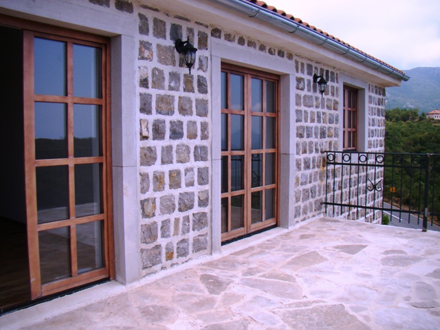 Karadağ, Petrovac’taki evin taş terası, panoramik ahşap kapılar ve dağ manzarası.