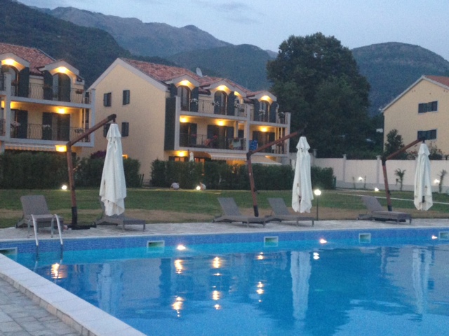Budva, Karadağ’daki konut kompleksinde şezlonglu açık yüzme havuzu, akşam saatlerinde dağlar arka planda.
