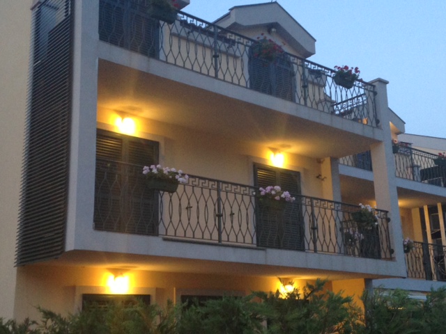 Karadağ, Budva’daki konut binasının cephesi: ferforje korkuluklu, çiçekli ve akşam aydınlatmalı şirin balkonlar.